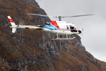 white and red helicopter flying near mountain terrain during daytime