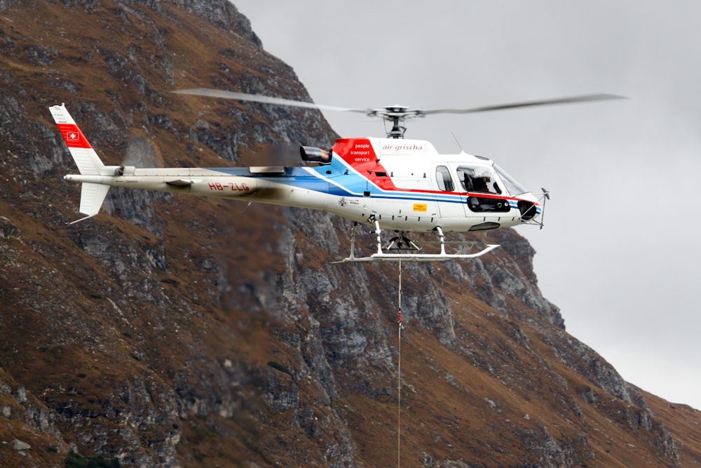 Weißer und roter Hubschrauber, der tagsüber in der Nähe von Berggelände fliegt