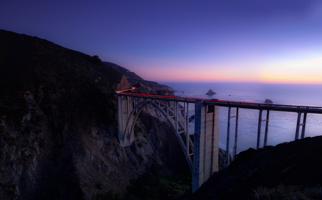 grey concrete bridge between brown and black cliff near body of water during night time