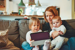 two babies and woman sitting on sofa while holding baby and watching on tablet