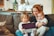 two babies and woman sitting on sofa while holding baby and watching on tablet