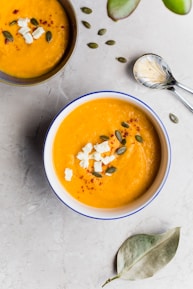 two bowls of orange soup topped with seeds