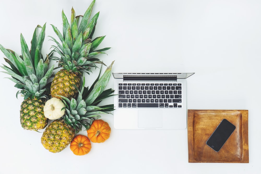 frutas de piña cerca de MacBook en superficie blanca