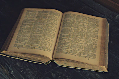 An open old book with worn pages resting on a wooden table.
