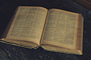 Ancient tome opened on a wooden table with faded maps around.