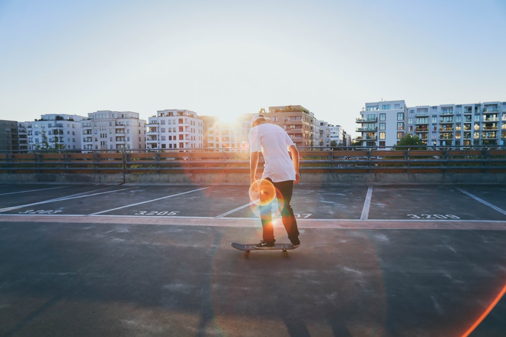 Mann fährt Skateboard auf dem Parkplatz in der Nähe von Gebäuden während der goldenen Stunde