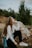 woman sitting on rock near green tree under white clouds and blue sky