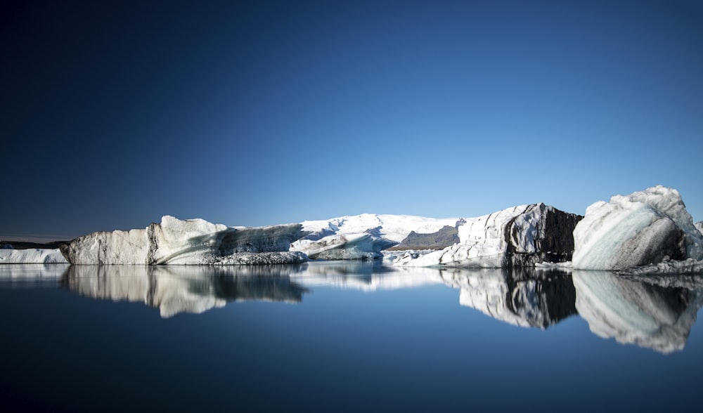 Montagna nera coperta di neve vicino allo specchio d'acqua durante il giorno