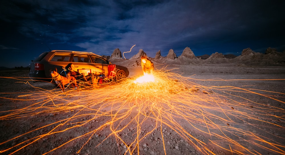 person sitting beside car under cloudy sky