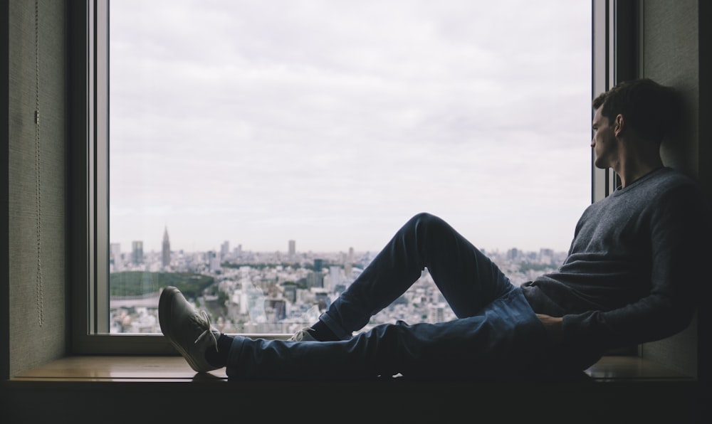 man sitting on brown wooden windowsill across buildings