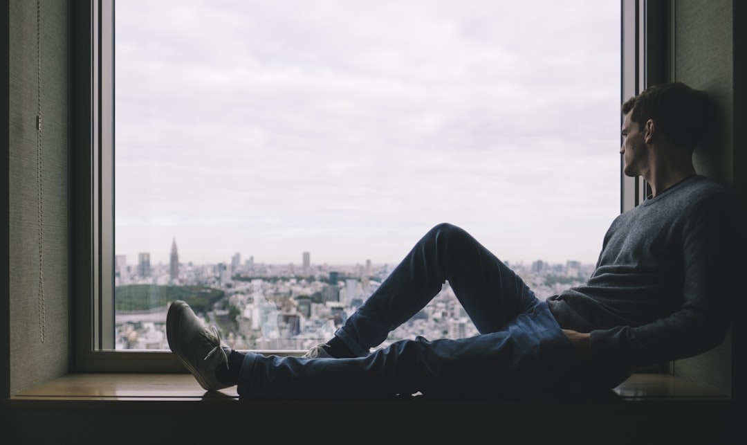 man sitting on brown wooden windowsill across buildings,