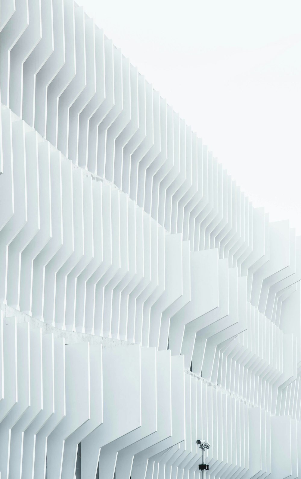 A security camera near parallel white ribs in a building facade in Madrid