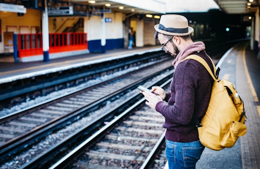 man using phone while standing in front of train rail during daytime