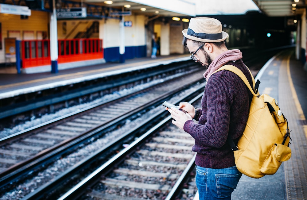 man using phone while standing in front of train rail during daytime