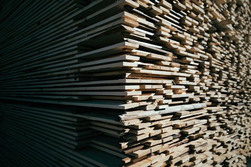 Stacks of neatly arranged timber planks in a sunlit warehouse.