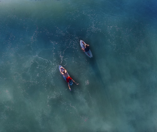 top view photography of two persons on blue surfboard at daytime