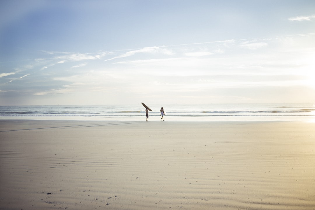two person standing on seashore under clear blue sky, Heading into the surf