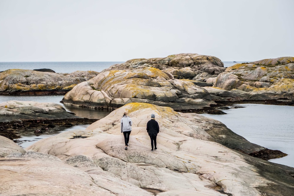 donna e uomo che camminano sulla formazione rocciosa vicino allo specchio d'acqua durante il giorno