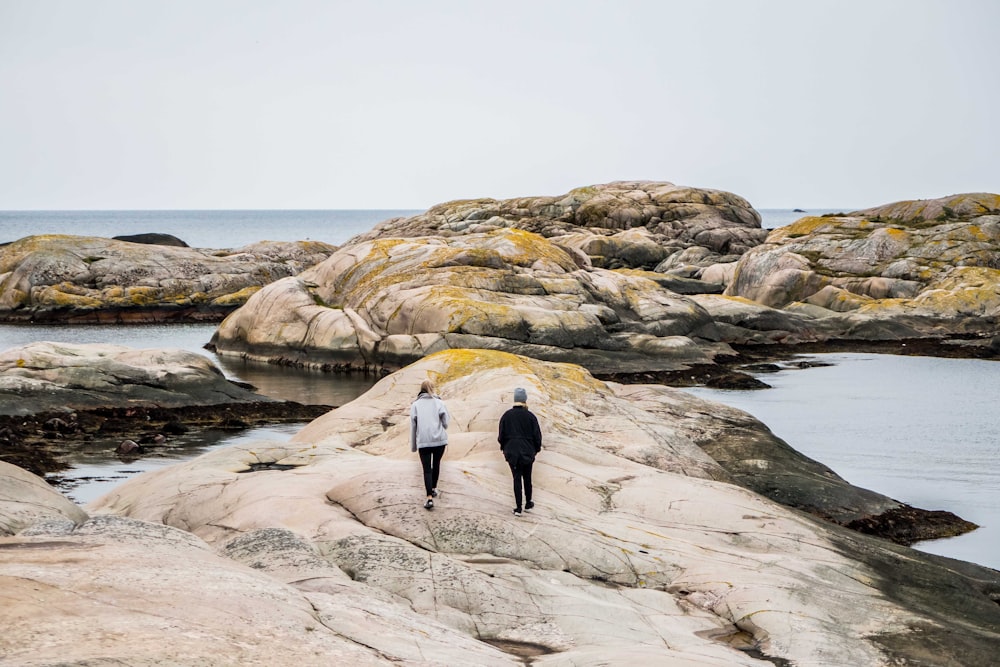woman and man walking on rock formation near body of water during daytime