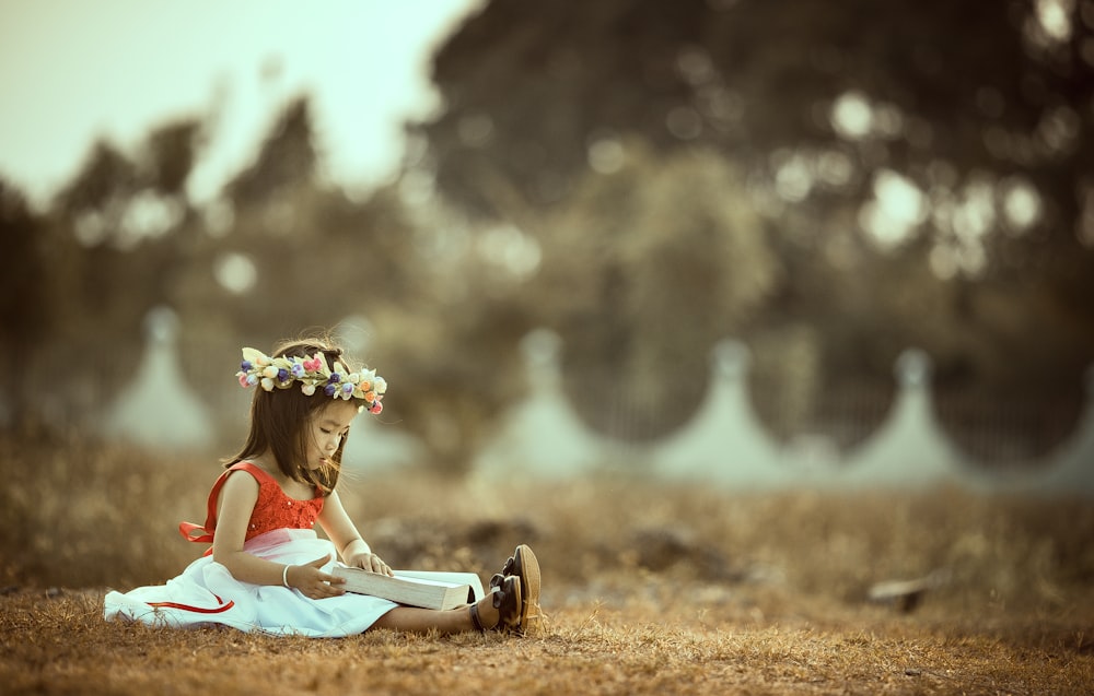 girl sitting whil holding book on field
