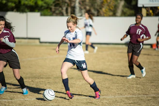 Young players in blue jerseys practicing dribbling drills on a sunny soccer field.