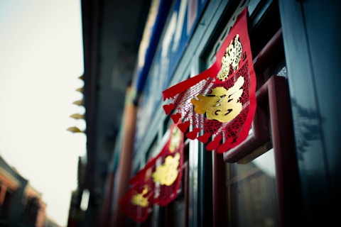 Red and gold decorative banners are displayed with intricate patterns, likely associated with Chinese New Year or a festive celebration. The banners are attached to a window, with a soft focus effect on the background, creating a sense of depth.