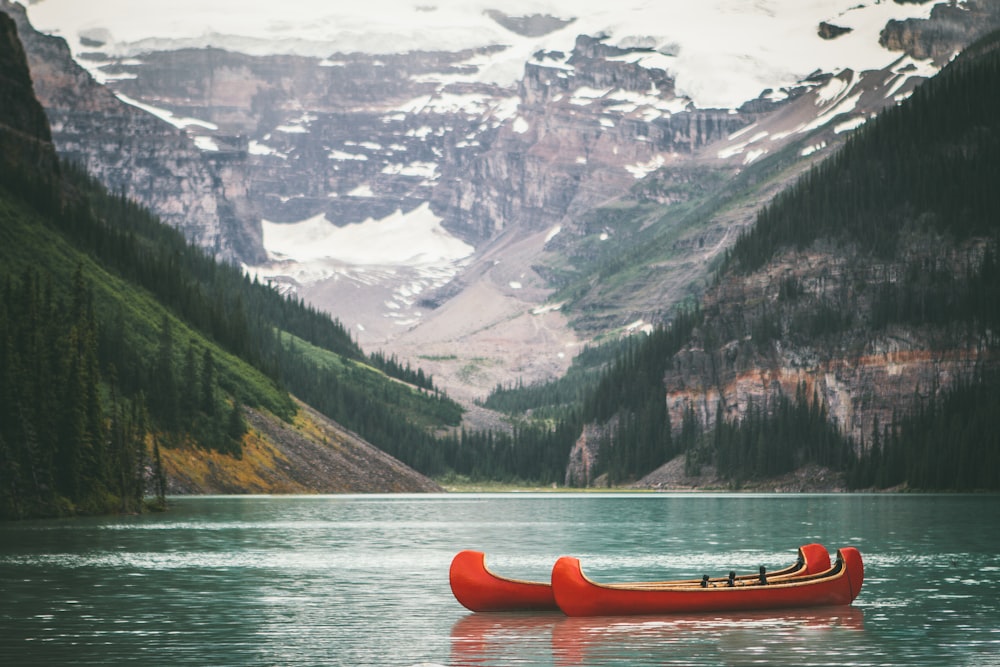 two orange boats on body of water in front of mountain with trees during daytime