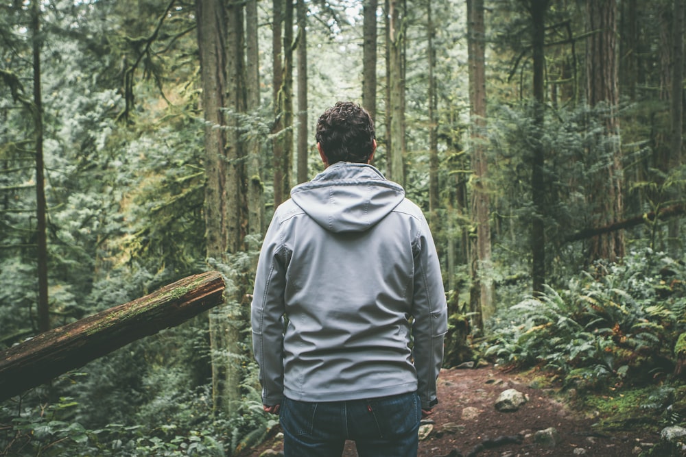 man in gray hooded jacket standing on dirt road between trees during daytime