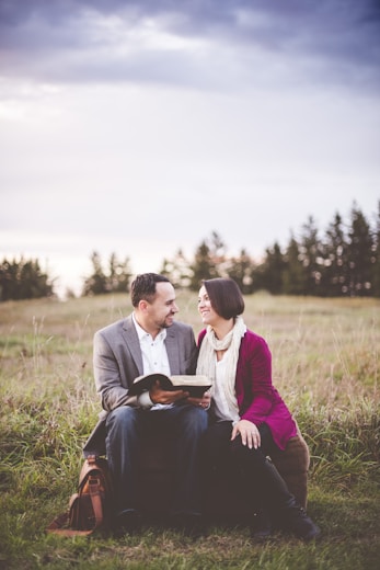 photo of man reading book to woman under grey cloudy sky