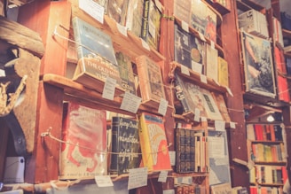 A cozy, dimly lit bookstore with wooden shelves filled with various books. Handwritten notes and tags are attached to the shelves, adding a charming and personal touch. Some of the books have classic, recognizable titles, and sunlight filters gently into the space.
