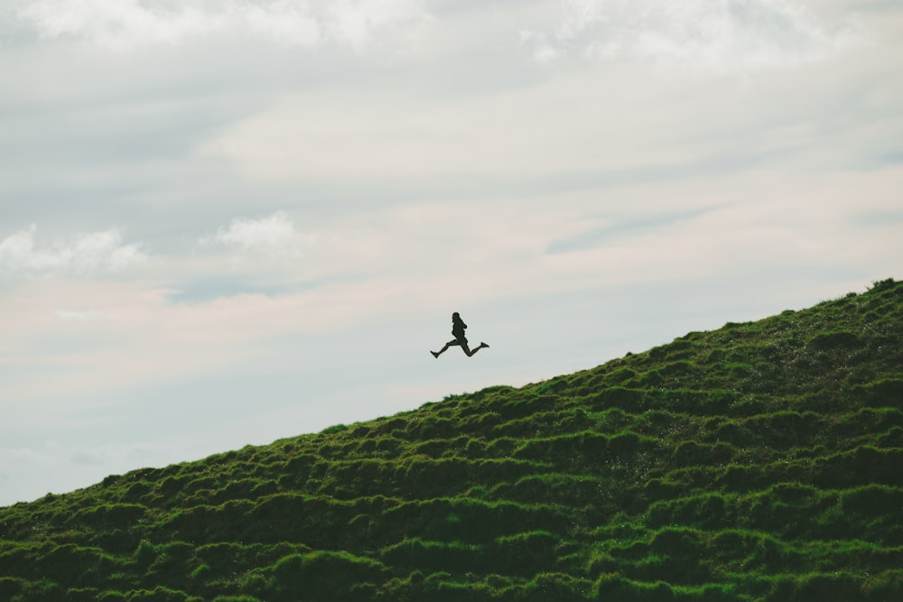 昼間、曇り空の下、草原で飛び跳ねる人