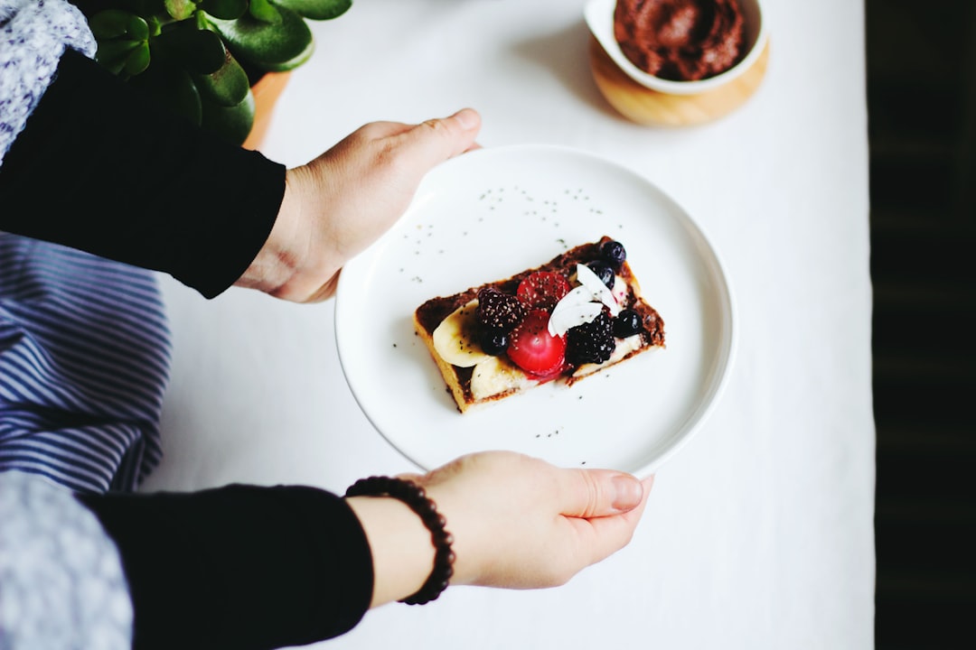 A person holding a plate of toast with jam, berries, bananas, and almonds