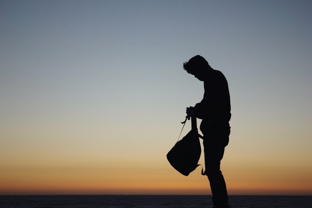 Silueta de hombre sosteniendo mochila durante la puesta de sol naranja