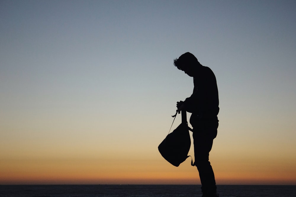 silhouette di uomo che tiene lo zaino durante il tramonto arancione