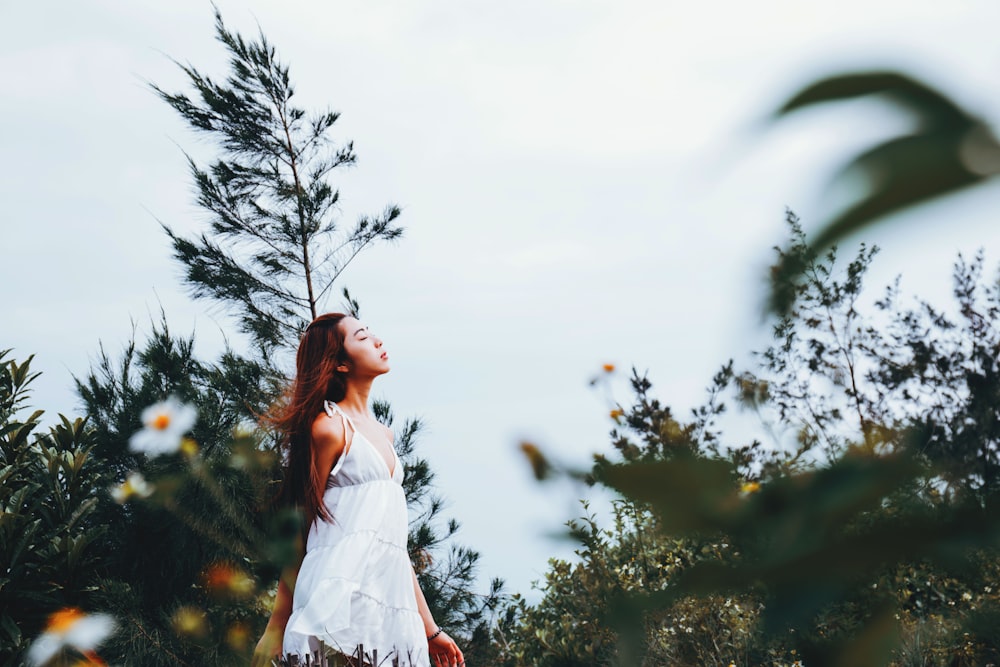 mulher no vestido branco profundo V-neck sem mangas cercado com plantas