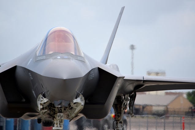 A modern, sleek fighter jet is positioned on the ground, with its sharp, angular design in full view. The cockpit canopy is slightly tinted, and the aircraft's sophisticated engineering is evident in its structure and landing gear.
