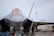 A modern, sleek fighter jet is positioned on the ground, with its sharp, angular design in full view. The cockpit canopy is slightly tinted, and the aircraft's sophisticated engineering is evident in its structure and landing gear.