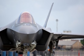 A modern, sleek fighter jet is positioned on the ground, with its sharp, angular design in full view. The cockpit canopy is slightly tinted, and the aircraft's sophisticated engineering is evident in its structure and landing gear.