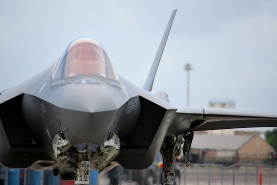 A modern, sleek fighter jet is positioned on the ground, with its sharp, angular design in full view. The cockpit canopy is slightly tinted, and the aircraft's sophisticated engineering is evident in its structure and landing gear.