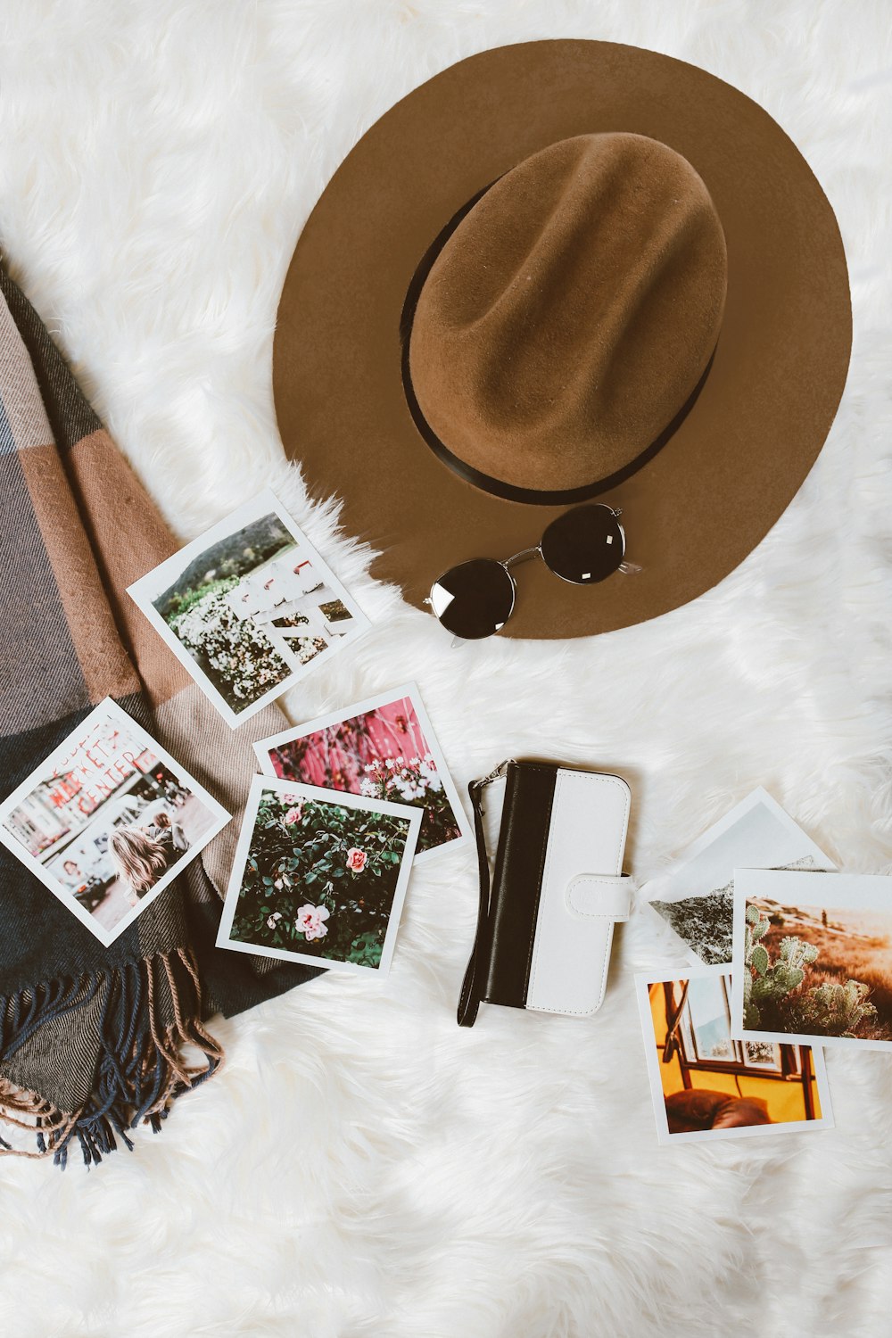 gold-colored framed sunglasses on brown hat beside white and black leather wristlet surrounded by photos on white and gray floral textile