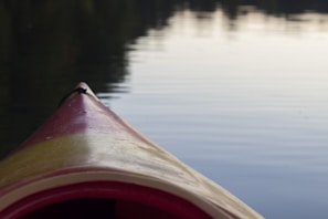 Close-up of a kayak gliding across crystal-clear water with reflections of autumn-colored trees