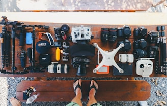 person standing near black and white quadcopter drone near cameras on brown wooden table