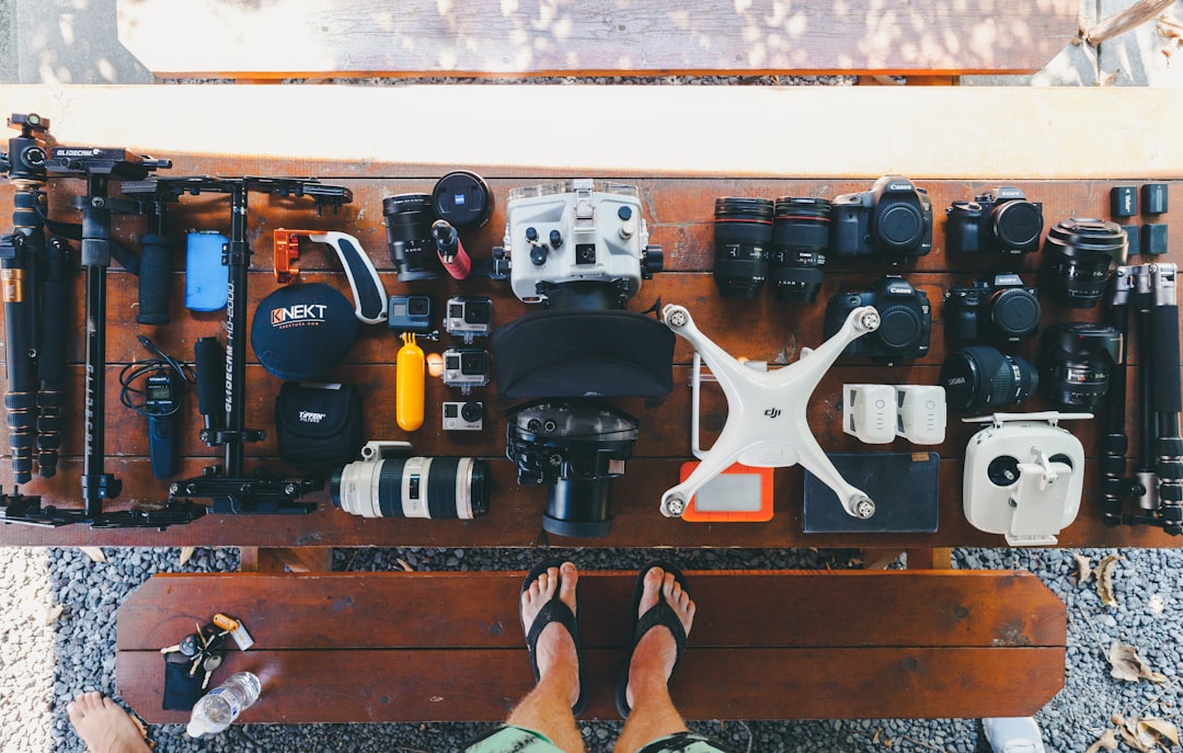 person standing near black and white quadcopter drone near cameras on brown wooden table, Photography equipment flatlay