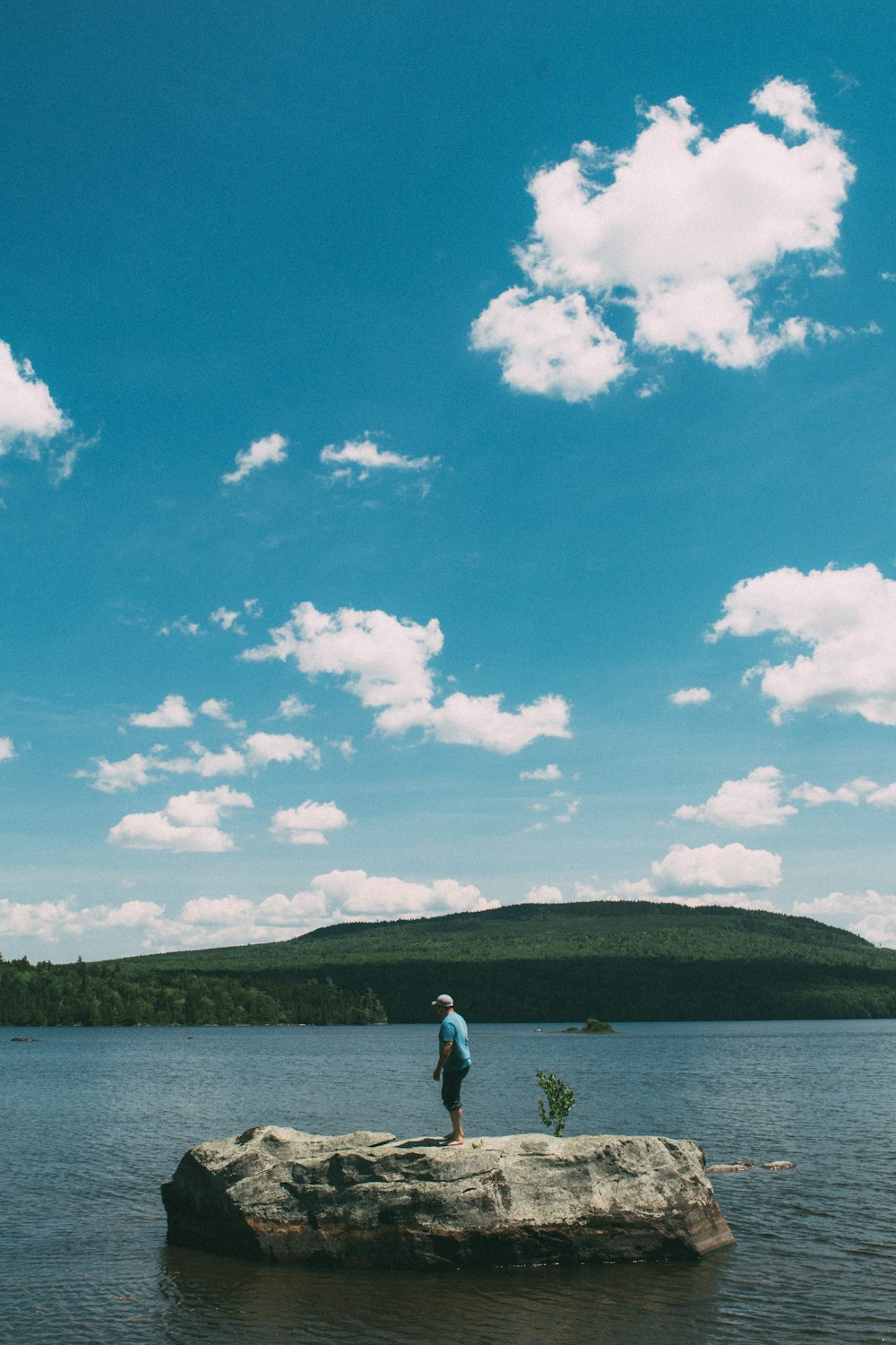 Mann in weißem Hemd und blauen Jeans steht am Meeresufer unter blau-weißen Wolken
