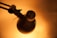 A close-up view of a metal lamp head with perforations, casting a warm orange glow. The arm of the lamp is visible and appears metallic and adjustable with screws and joints.