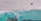 Aerial view of a large turquoise body of water adjacent to a sandy, barren landscape with visible tire tracks, and a construction vehicle near the edge. The scene embodies a contrast between the serene water and the structured, industrialized land.