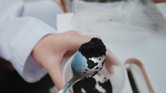 A person holding a spoonful of shilajit over a cup of warm water.