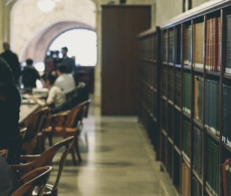 selective focus photography of books on bookcases near people sits in chairs