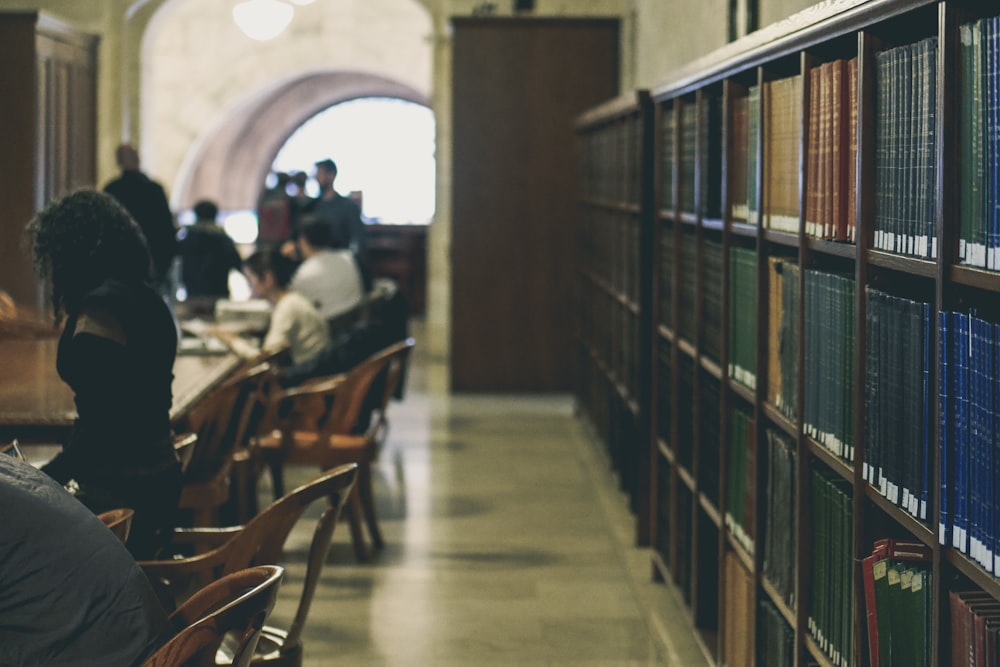 selective focus photography of books on bookcases near people sits in chairs