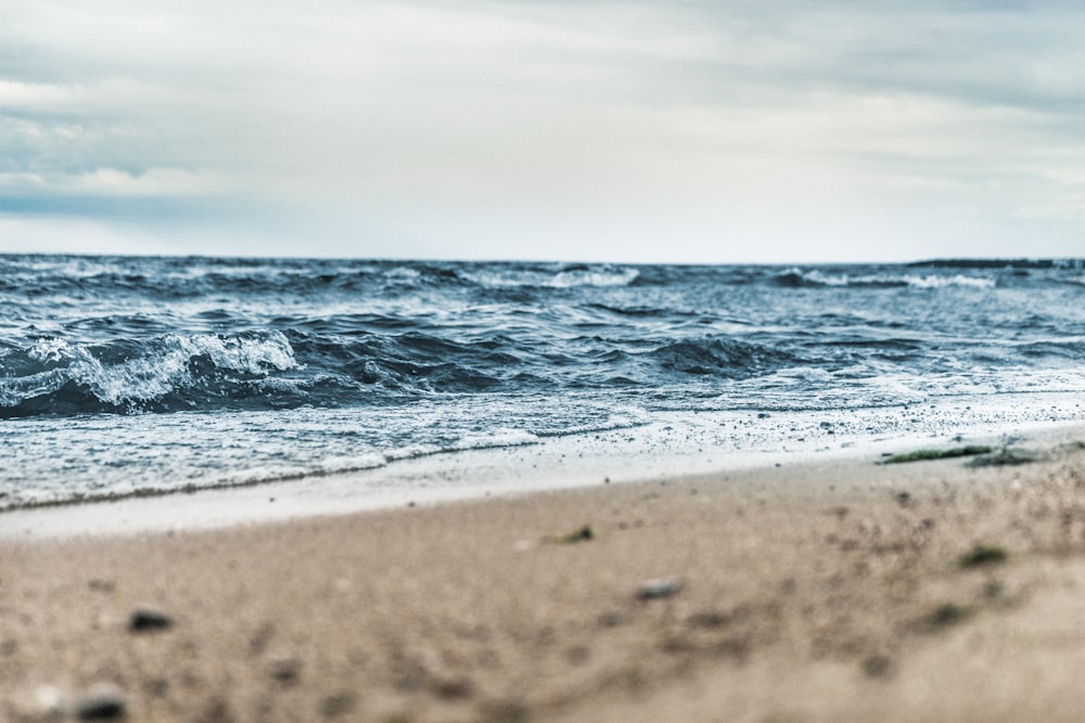 Photographie en contre-plongée de sable brun à côté d’un plan d’eau sous un ciel blanc et bleu de jour